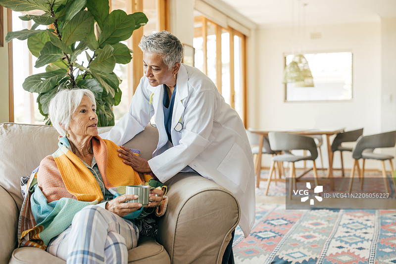 一位老年女性在护士的帮助下，享受着温暖的宁静早晨，手中端着茶。图片素材