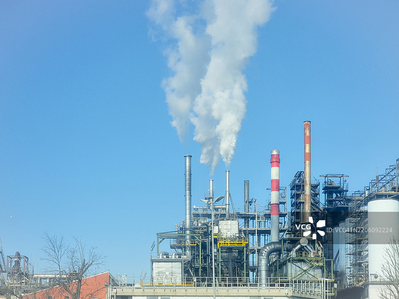 拉文纳附近的工业景观：烟雾弥漫的烟囱、管道和建筑在晴朗的蓝天下，捕捉到2025年3月意大利制造中心的精髓图片素材