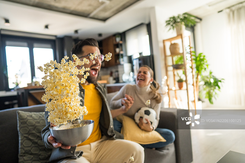 一对情侣在电视上观看现场直播的足球盛宴，沉浸在快乐中。图片素材