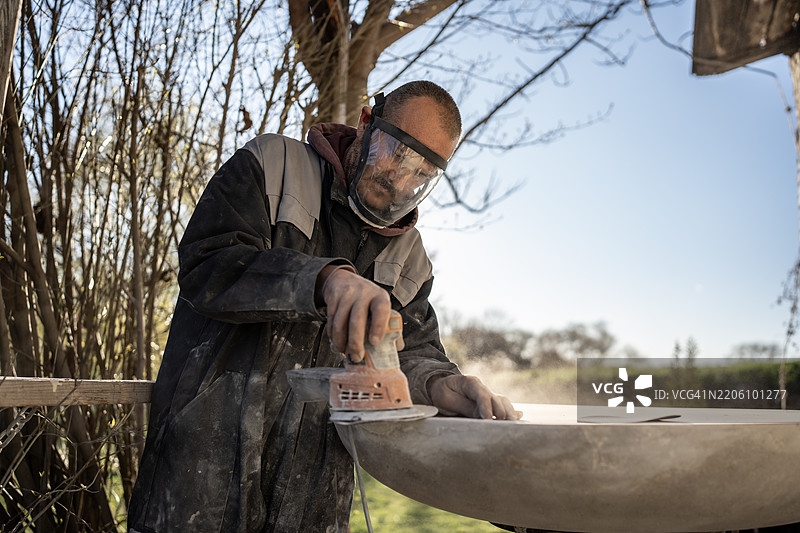 在阳光明媚的户外，男子正在打磨一个大型物体图片素材