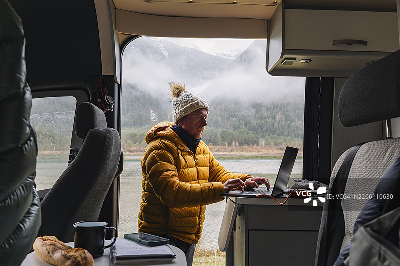 一位成熟的男士在比利牛斯山的湖边的露营车内，趁着下雨的冬日补做一些工作。图片素材