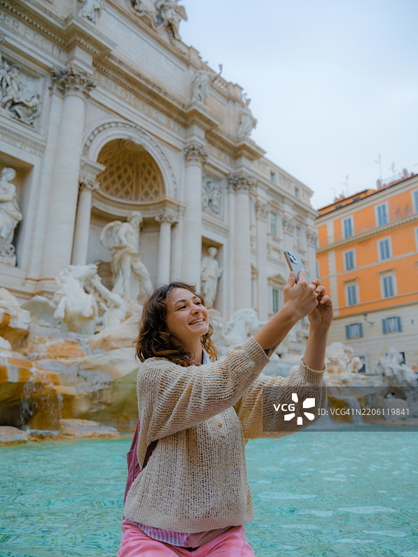 在罗马特雷维喷泉附近用智能手机拍照的女性图片素材