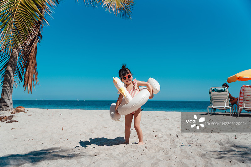 可爱的亚洲小女孩在海滩上玩耍，身旁有一个充气天鹅游泳圈。图片素材