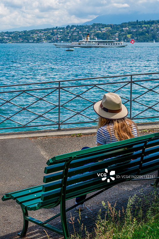 一位女性背对着坐在日内瓦湖边的长椅上。图片素材