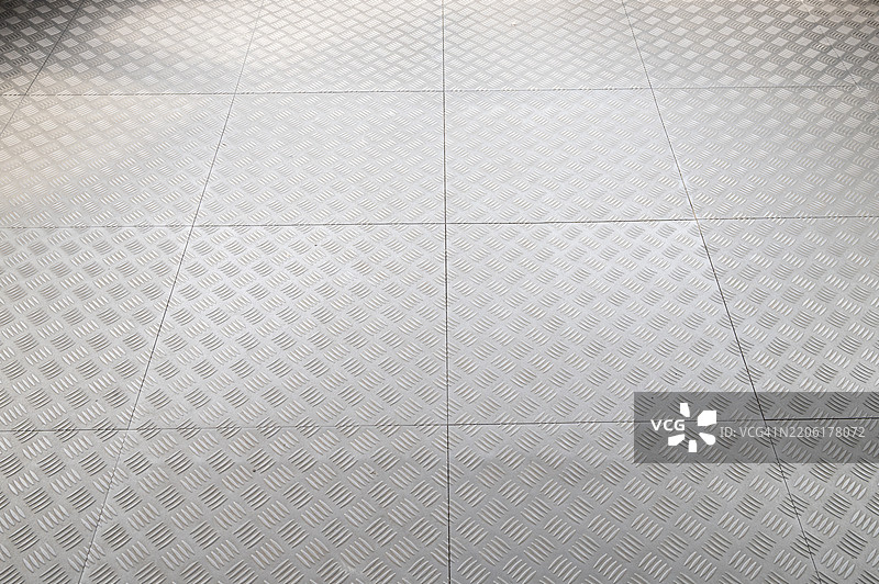 钢制菱形板的特写。金属的纹理清晰可见，凸起的菱形形状增强了工业感。菱形板通常用于地板、人行道和其他需要防滑表面的应用。图片素材