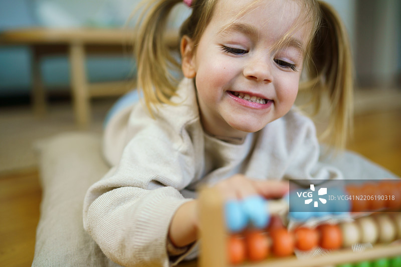快乐的女孩在家里躺着玩算盘玩具图片素材