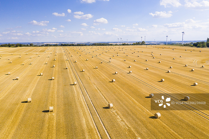 从上方俯瞰收割后的谷物田中的稻草 bale，背景是风力涡轮机，德国萨克森州诺森，欧洲图片素材