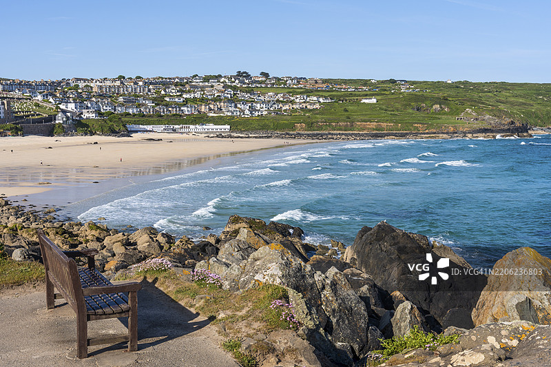 圣艾夫斯和波斯莫尔海滩的景色，海洋和沙滩尽收眼底，前面有一张长椅。圣艾夫斯，康沃尔，英格兰，英国图片素材
