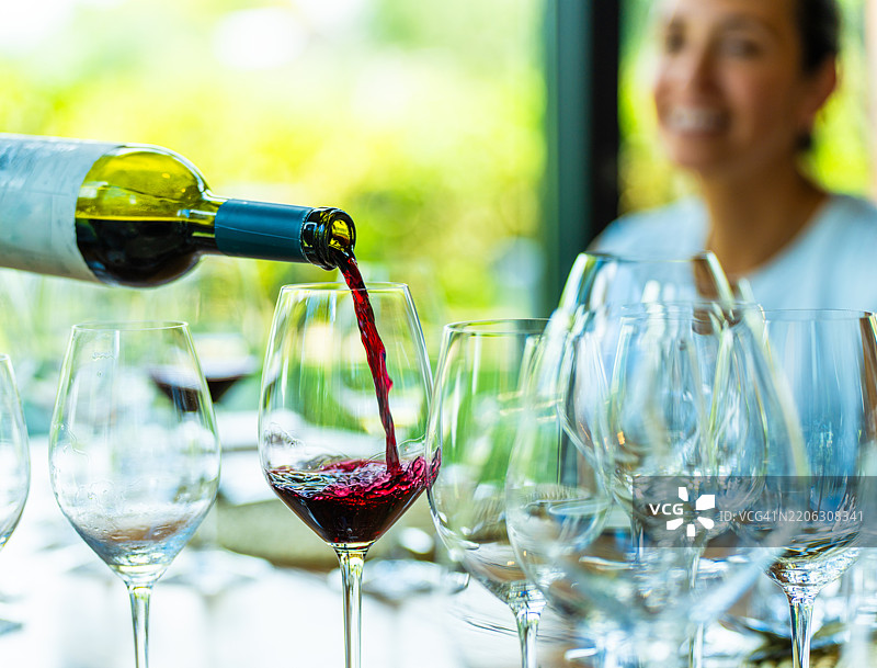 一位侍酒师为一位快乐的女性倒了一杯梅洛红酒图片素材