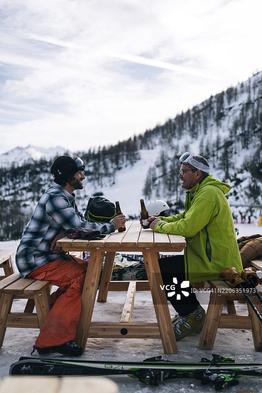 父亲和成年儿子在瑞士滑雪胜地享受啤酒图片素材