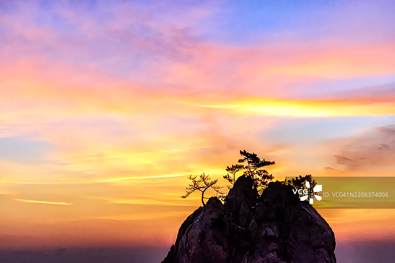 树木映衬下的轮廓分明的岩石山丘与绚丽的天空图片素材