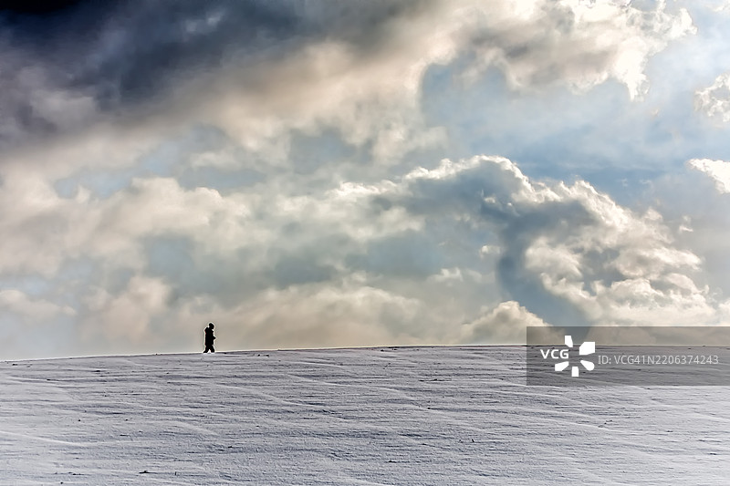 一个人在云雾弥漫的天空下，走在覆盖着白雪的山丘上图片素材