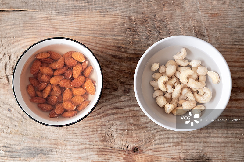 浸泡在温水中的杏仁和腰果，放在白色碗里，背景为木质桌面图片素材