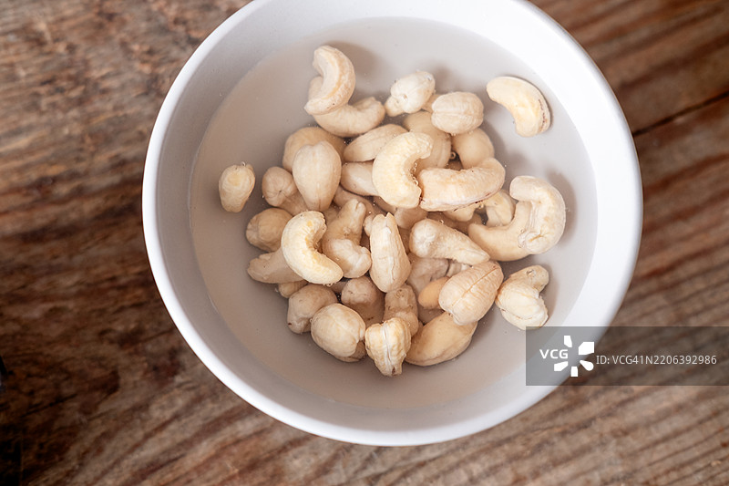 浸泡在温水中的腰果，放在白色碗里，背景为木质桌面图片素材