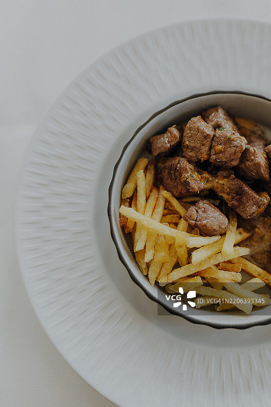 香嫩牛肉块配脆薯条，盛在白色盘子里图片素材