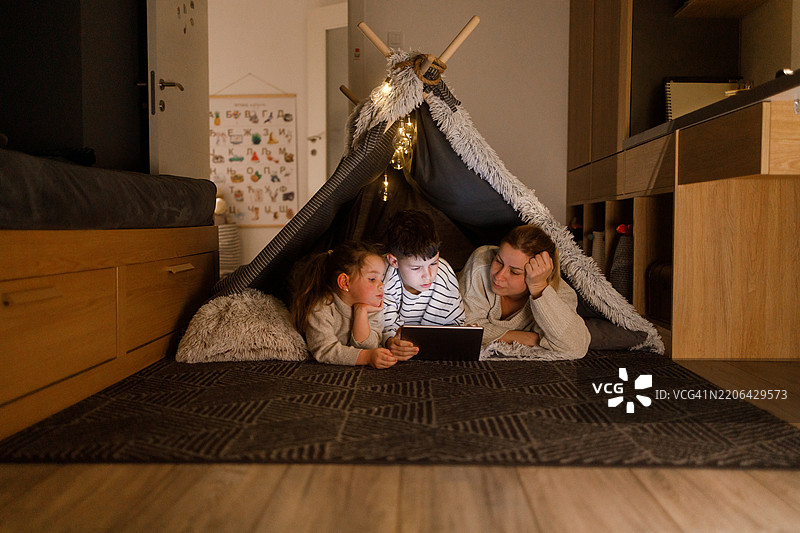 在温馨的毯子堡中，家庭成员们与数字平板一起亲密互动图片素材