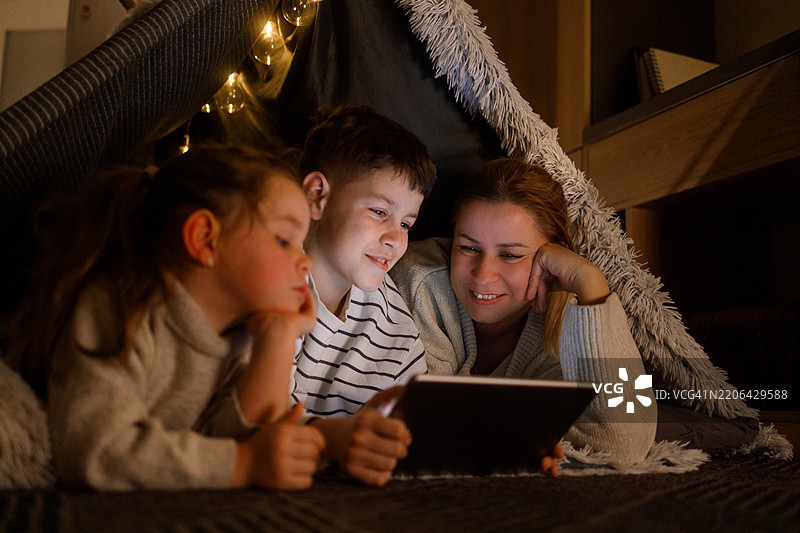 在舒适的毯子堡中，家庭成员们与数字平板一起增进感情图片素材