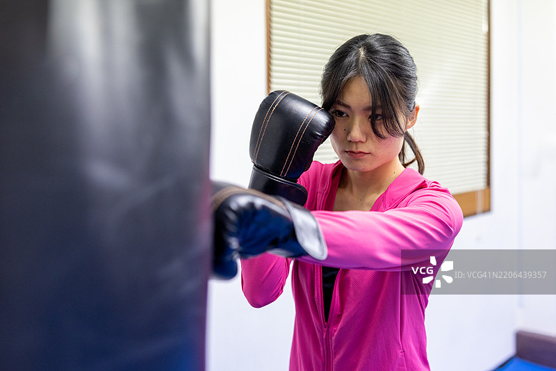 女性运动员在健身房训练拳击 - 击打沙袋图片素材