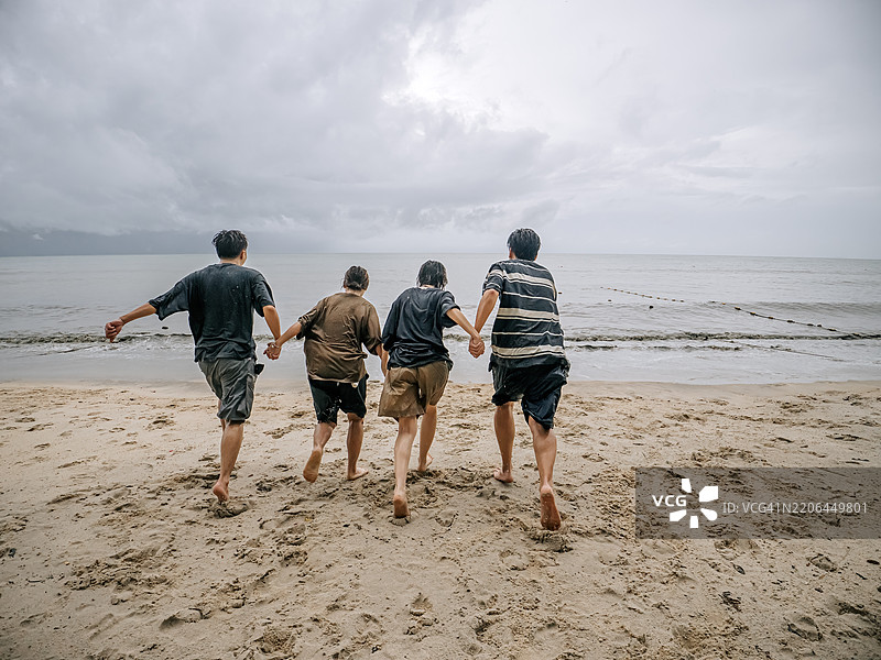 背影的亚洲中国朋友们在槟城岛的雨天奔向大海，享受海滩假期。图片素材