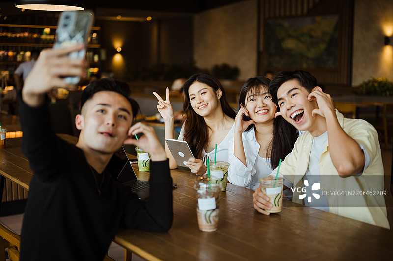 一群迷人的亚洲朋友在咖啡馆一起聚会时拍自拍。图片素材