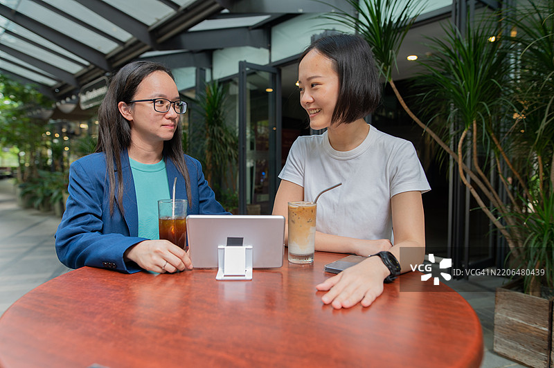 在咖啡店进行商务讨论的亚洲华裔女性，手持智能平板和饮品的照片图片素材