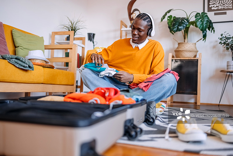 年轻男子在家中收拾行李箱，为旅行做准备，挑选衣物。图片素材