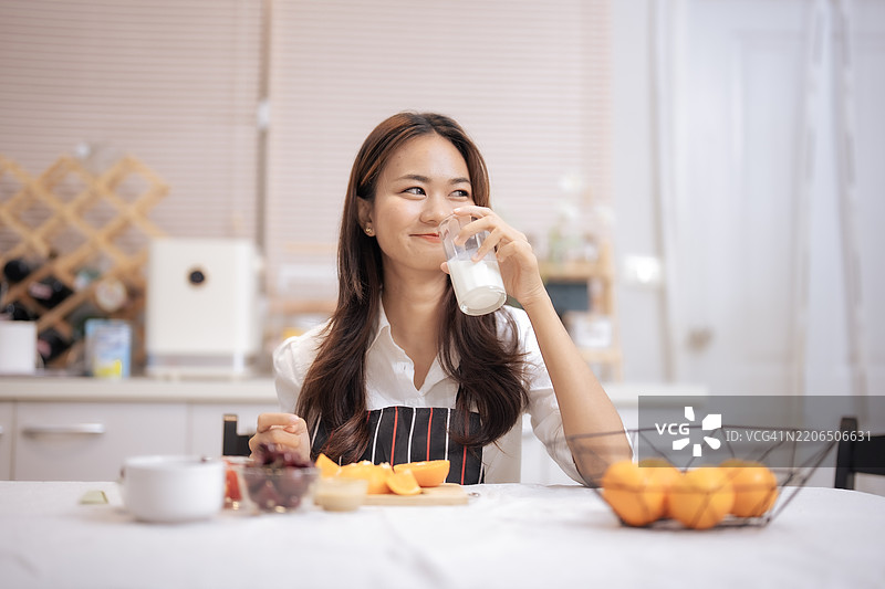年轻的亚洲女性在家中的厨房喝牛奶。人们享受健康生活方式的理念。图片素材