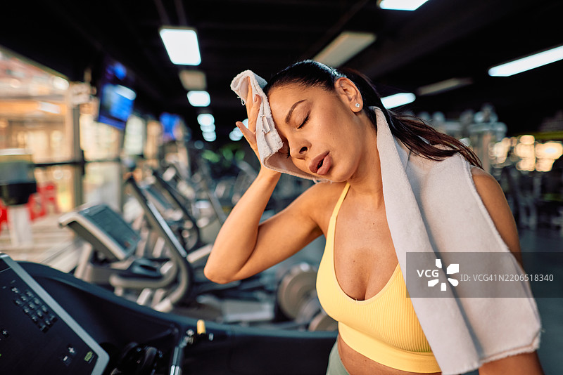 疲惫的女运动员在健身房训练后用毛巾擦汗图片素材