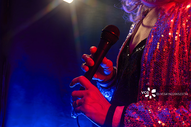 无法辨认的女性音乐家在霓虹灯照亮的舞台上演唱麦克风。图片素材