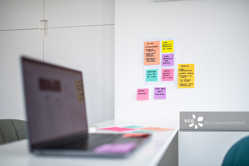 现代医生办公室白色墙壁上的彩色便签和笔记本电脑图片素材