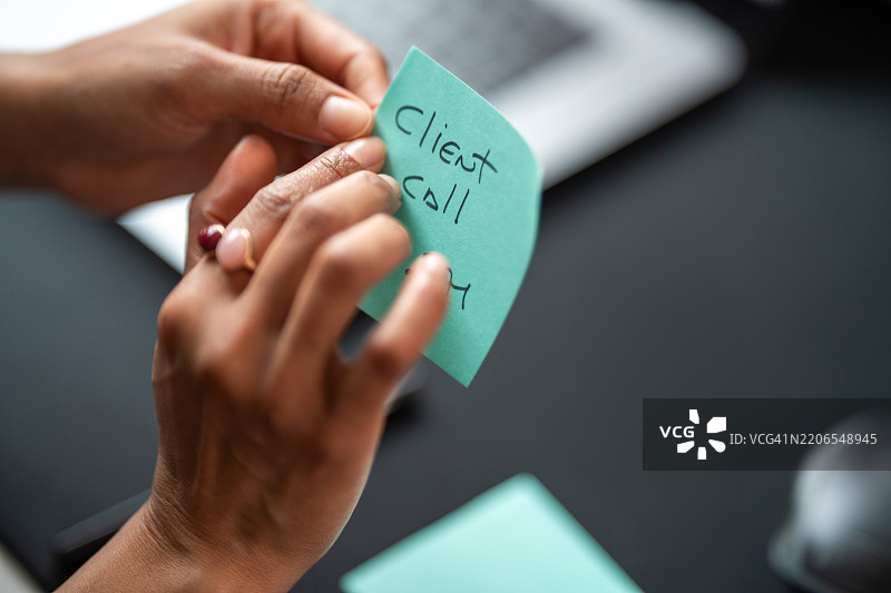 专业人士在现代办公室的青绿色便签上写下客户电话提醒图片素材