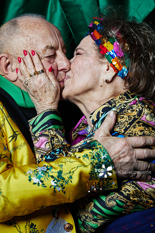 一对穿着传统服饰的老年夫妇手牵手，亲吻在一起。图片素材