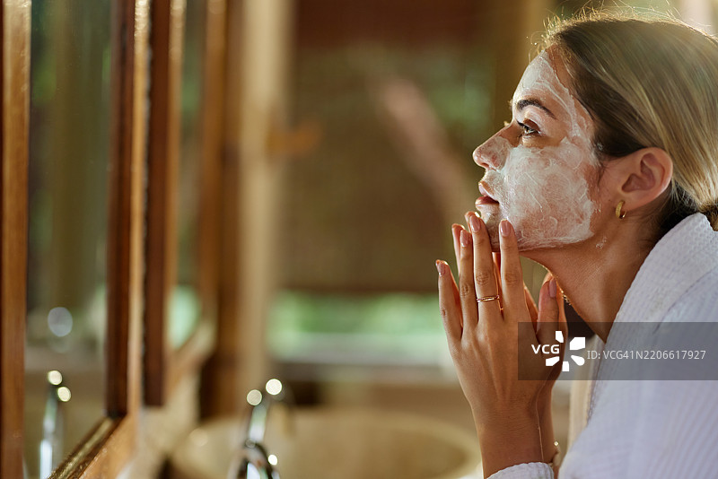 美丽的女人在浴室里涂抹面霜。图片素材