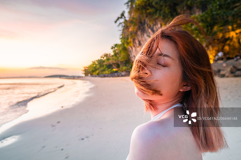 一位年轻女士在泰国克拉比省的Railay East海滩上站着，凝视着岩石，正值金色黄昏时分。图片素材