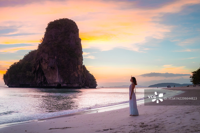 一位年轻女士在泰国克拉比省的Railay East海滩上站着，凝视着岩石，正值金色黄昏时分。图片素材