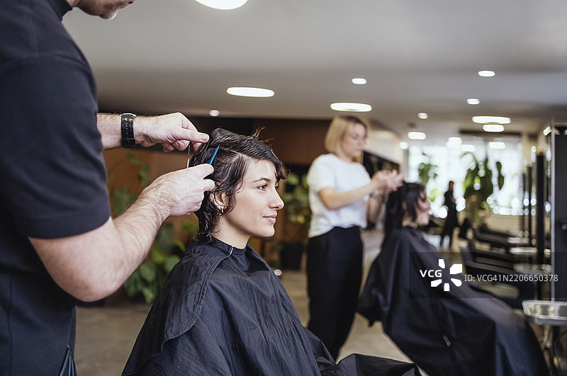 中年男性发型师在明亮现代的沙龙为女性顾客造型图片素材