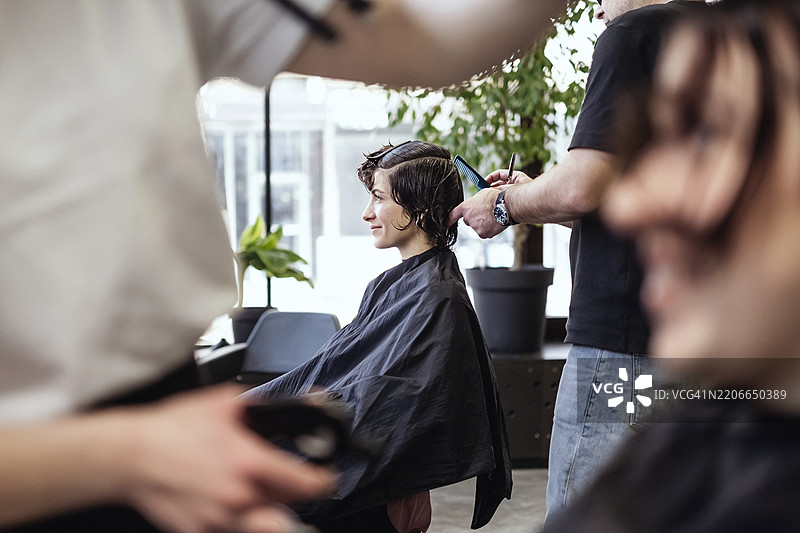 年轻女性在明亮现代的理发店里剪发，面带放松的表情图片素材