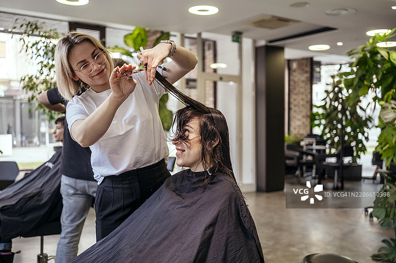 微笑的发型师在现代明亮的沙龙为女性顾客修剪湿发图片素材