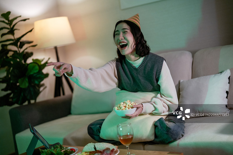 女人在沙发上放松，享受她最喜欢的节目，边吃爆米花，等待新年的倒计时。图片素材