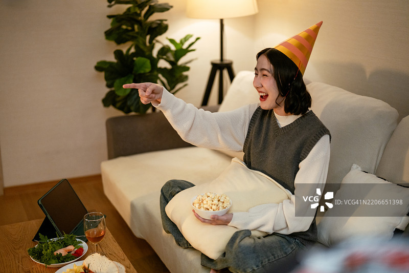 女人在沙发上放松，享受她最喜欢的节目，边吃爆米花，等待新年的倒计时。图片素材