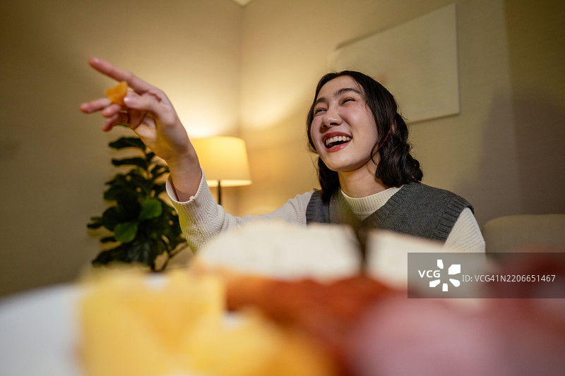 女人在沙发上放松，享受她最喜欢的节目，边吃爆米花，等待新年的倒计时。图片素材