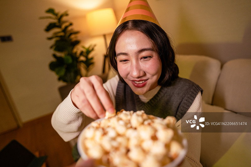 女人在沙发上放松，享受她最喜欢的节目，边吃爆米花，等待新年的倒计时。图片素材