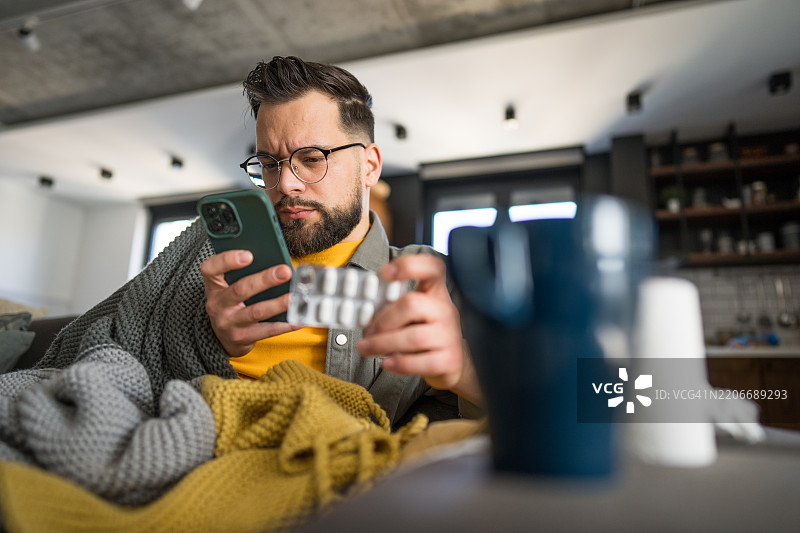 生病的男人在家用智能手机阅读药物说明书图片素材
