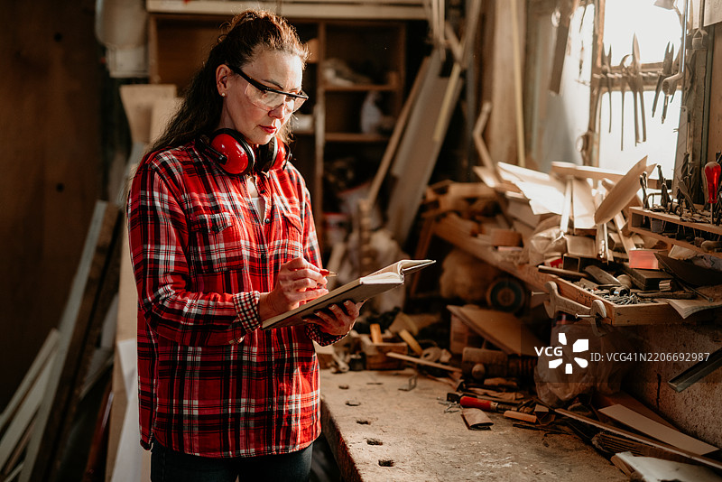 木匠在杂乱的工作坊里写笔记。图片素材