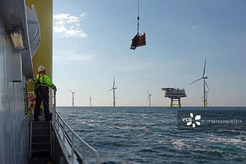 海上工人在船甲板上监督吊装作业。图片素材