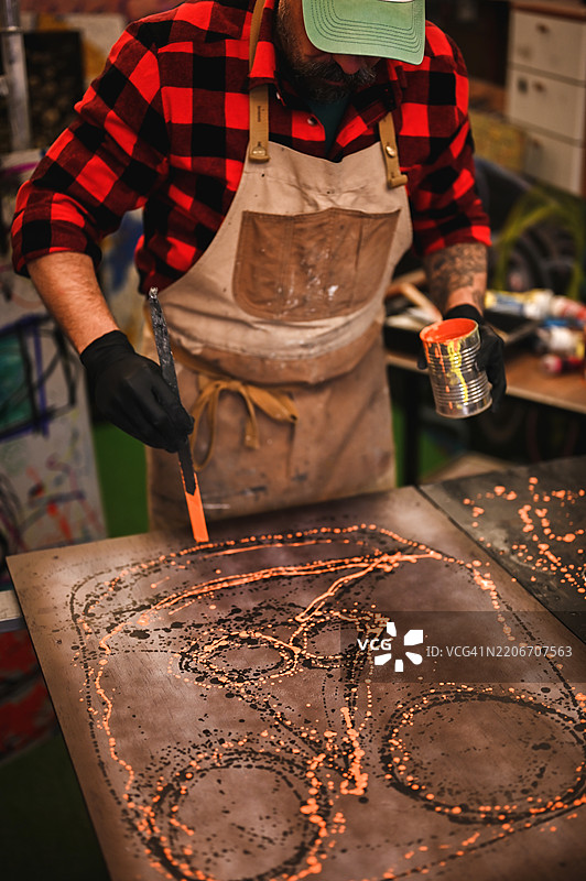 艺术家在工作室里小心地将橙色油漆涂抹在金属画布上图片素材