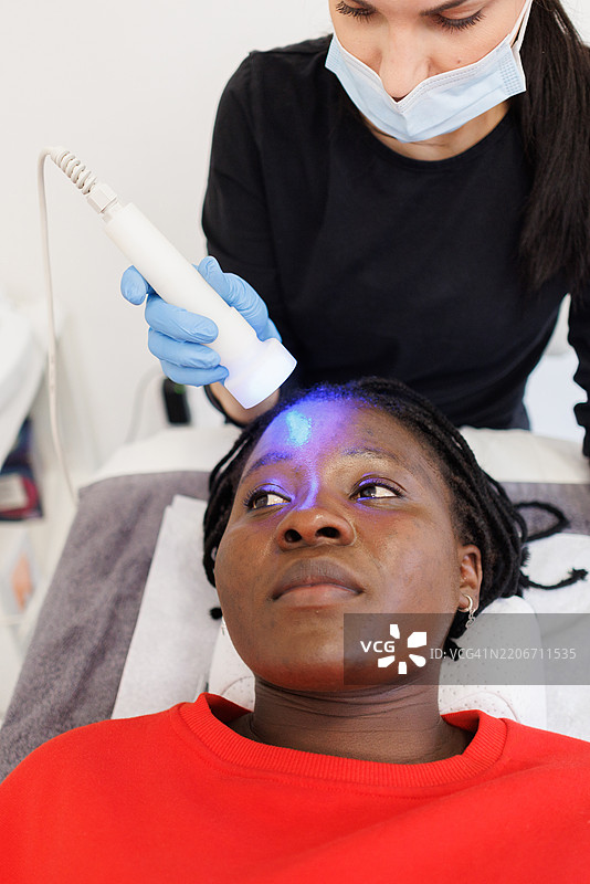 美容诊所中年轻黑人女性进行LED光疗会话图片素材
