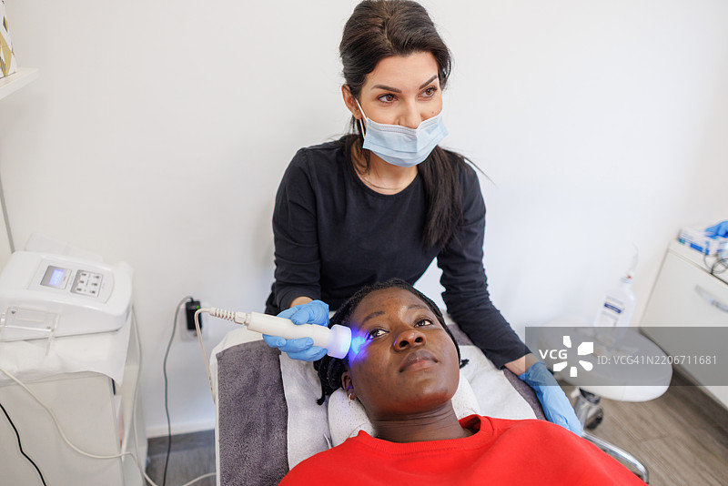 穿着黑色制服的护肤专家正在为客户进行LED光疗治疗图片素材