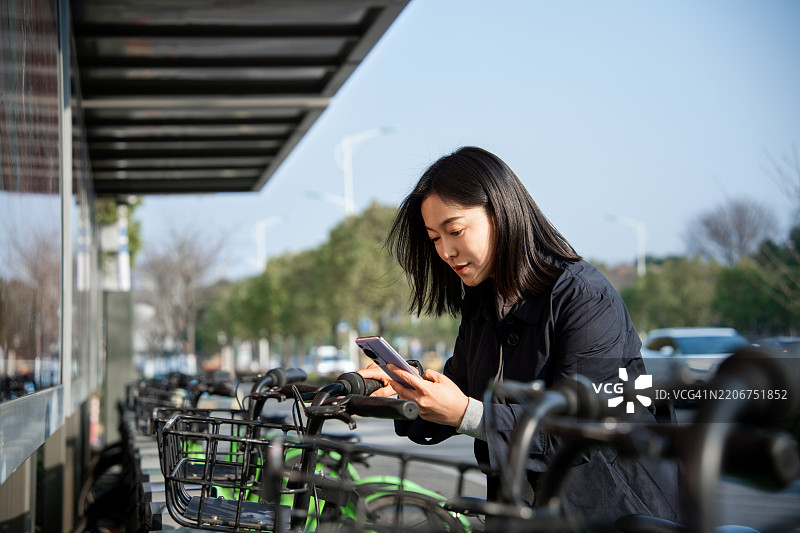 年轻亚洲女性在城市中使用智能手机租借共享自行车图片素材