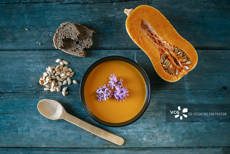 带花、种子、面包和木勺的南瓜汤放在乡村风格的桌子上图片素材